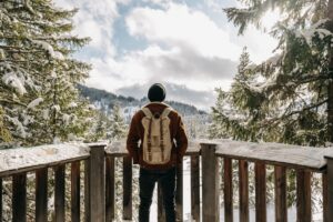 man-standing-front-wooden-fences-surrounded-by-hills-forests-covered-snow.jpg